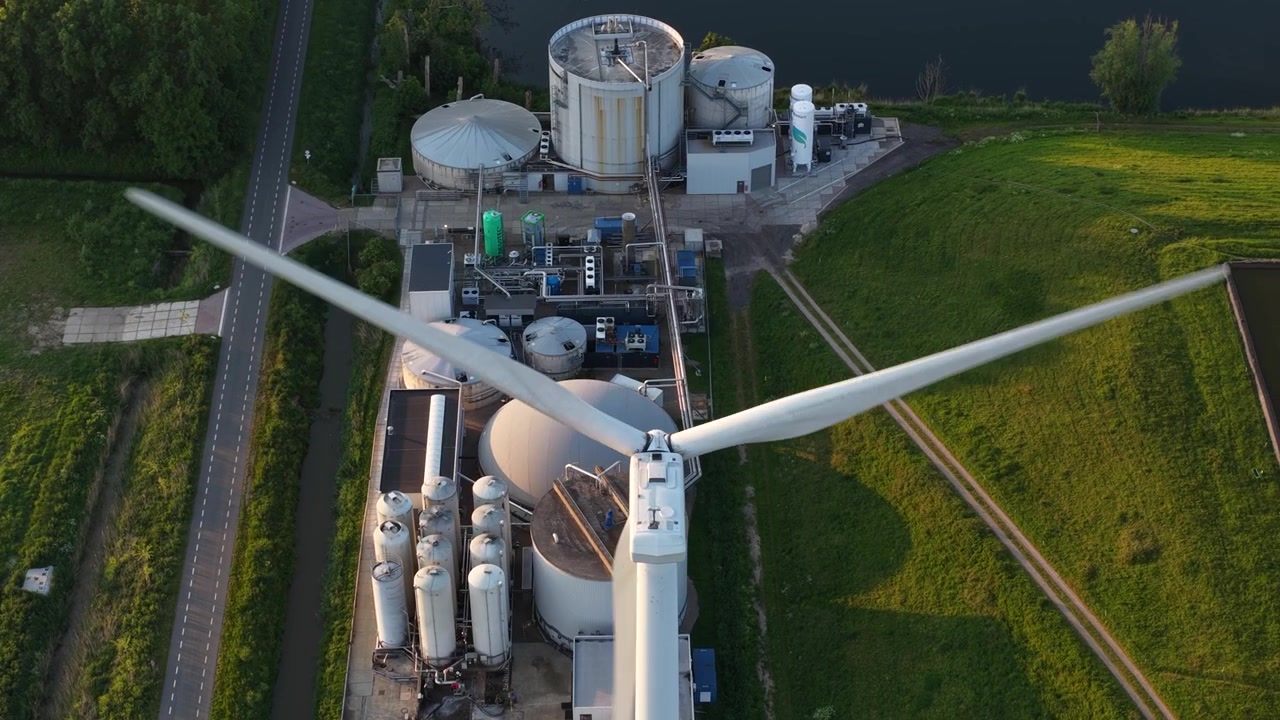 Stunning aerial top down view of a modern wind turbine with rotating blades, located next to a biogas facility, highlighting the combination of renewable energy sources in a rural setting