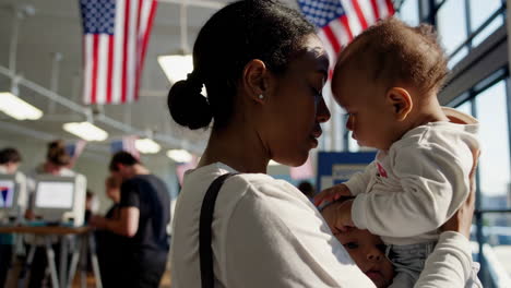 woman holding a baby at a polling station with american flags