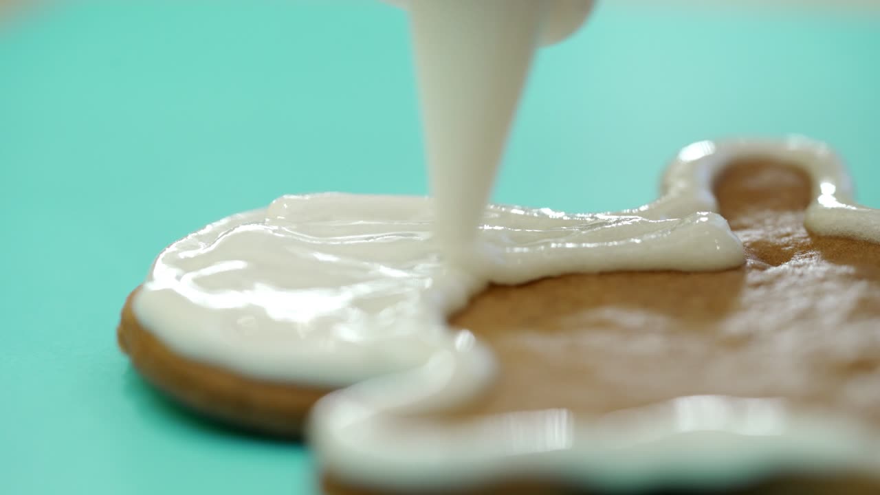 Surface of tasty gingerbread is filling by white glaze. Gingerbread cookie covering by white icing on the blue background. Close-up