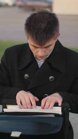 직장 후 야외에 앉아있는 사업가, 도시 환경에서 문서를 검토하고, 배경에 사무실 건물, 거리 조명 및 황혼에 주차 된 자동차