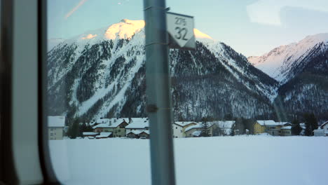 Snowcapped-Swiss-Alps-and-mountain-village-from-inside-Glacier-Express-in-Switzerland