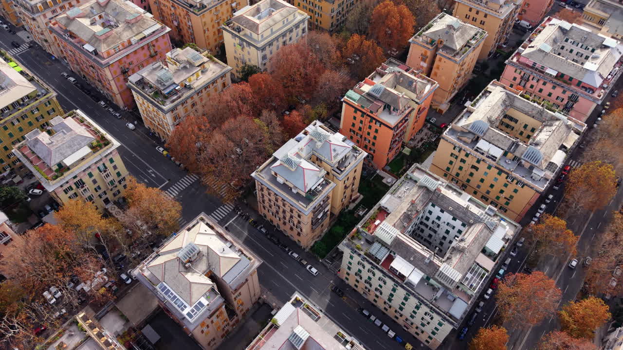 Panoramatický záběr dronu nad centrální Janovem zobrazující barevné obytné budovy, ulice lemované stromy, křižovatky a rušný městský provoz
