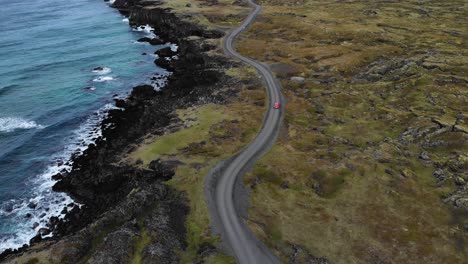 aerial of a red car driving on a bendy road at the coastline of iceland