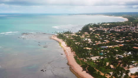 Vista-Aérea-De-La-Playa-Praia-Do-Forte,-El-Arrecife-De-Coral,-La-Zona-De-Palmeras-Y-La-Ciudad-Circundante,-En-Un-Día-Nublado,-Praia-Do-Forte,-Bahia,-Brasil