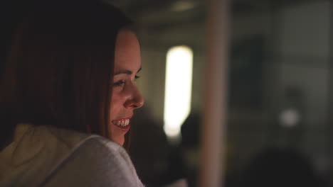 Close-Up-Of-Smiling-Woman-Sitting-On-Sofa-At-Home-At-Night-Streaming-Or-Watching-Movie-Or-Show-On-Laptop-Or-TV