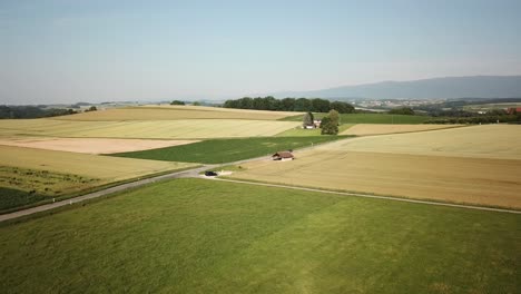 swiss countryside with different fields next to a road captured by drone, vaud