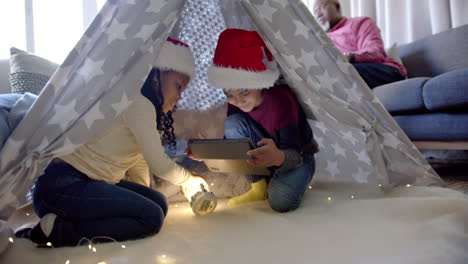 happy african american brother and sister in christmas hats with tablet in blanket tent, slow motion