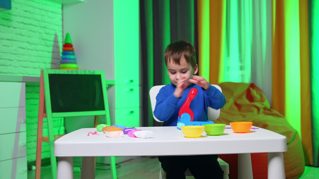 Adorable toddler kid plays with molding machine to sculpture from plasticine. Happy kid doing art hobby at home.