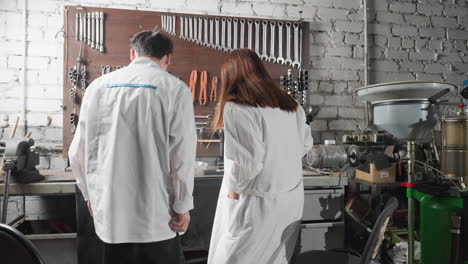 male and female technical specialists walk toward seat, sit down and adjust in an auto repair shop, wearing lab coats, with focus on chinese engineers designing automotive components