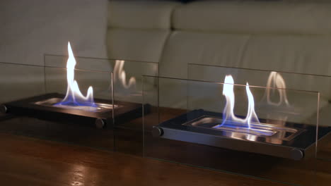 close up of indoor glass fronted fireplaces in a living room on a table with a sofa in the background of the room