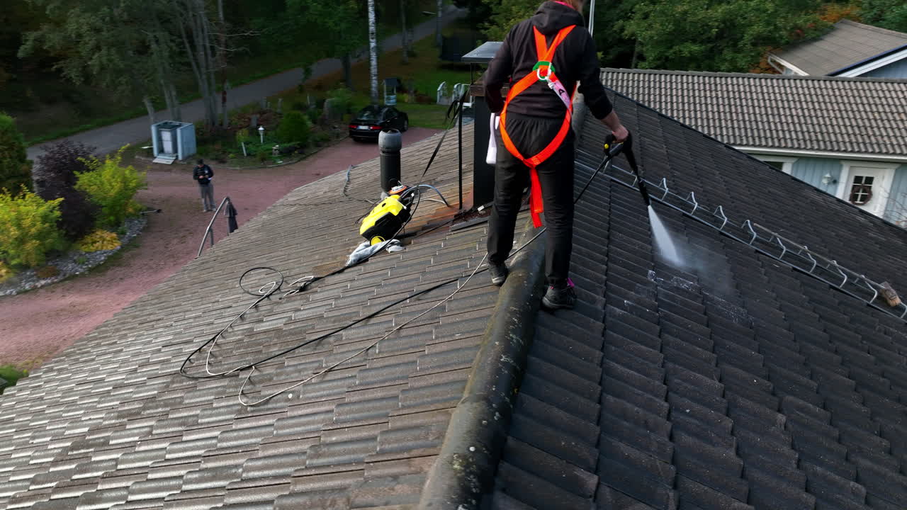 Drone filmer en kvinde, der vasker tagsten på et hus på en solrig efterårsdag