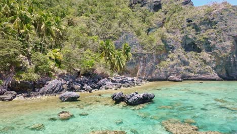 Aerial-view-showing-clear-water-with-rocks-and-coral-reef-at-tropical-palm-tree-landscape---Playa-Fronton,-Dominican-Republic