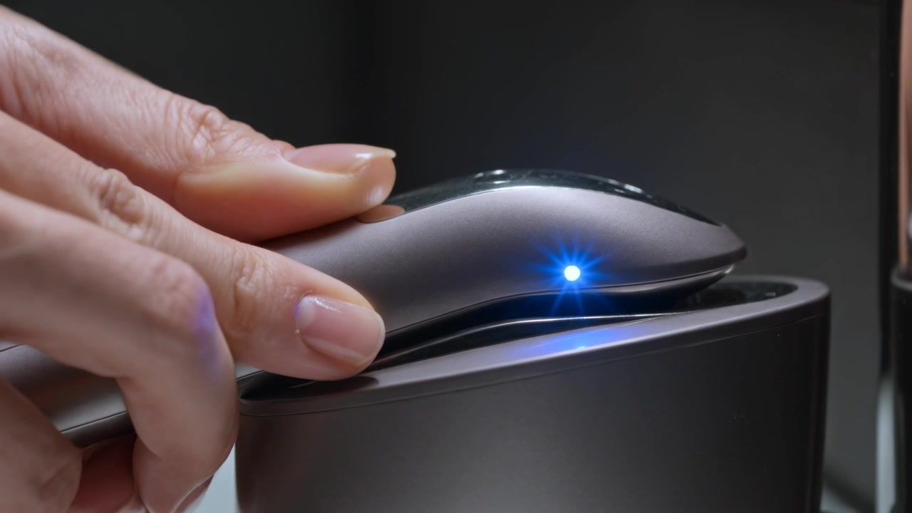 Una mano curata posiziona un dispositivo metallico in una base su una toeletta, con un LED blu che si illumina per la ricarica.