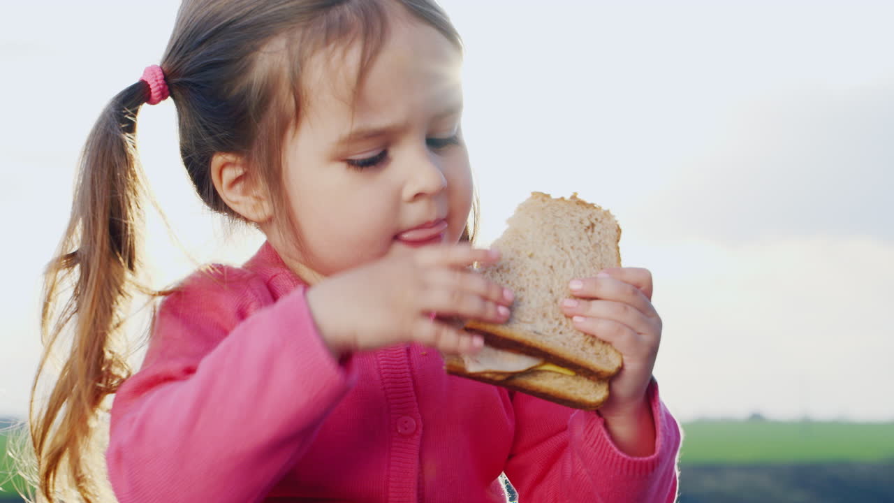 divertida niña de tres años comiendo un sándwich al sol al aire libre