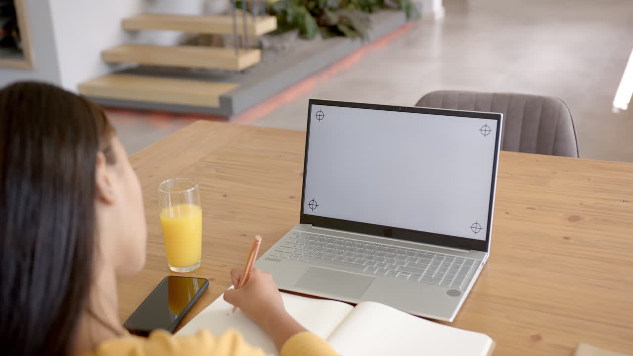 Writing in notebook, asian woman using laptop and smartphone at home with orange juice, copy space