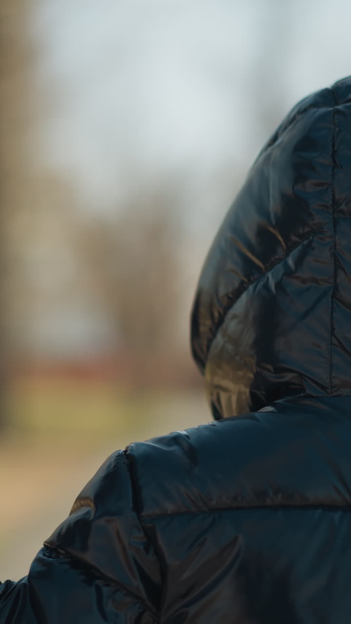 un primer plano de un niño que sostiene las manos de su padre mientras caminan juntos, ambos vestidos con chaquetas cálidas, con una vista borrosa de árboles en el fondo