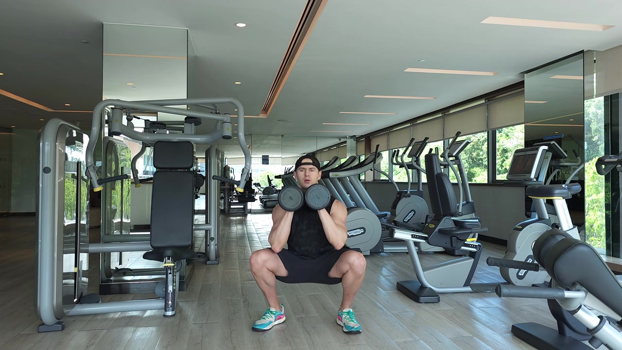 Uomo attivo che esegue squat con manubri nella palestra dell'hotel a Kota Kinabalu, Malesia. Inquadratura ampia