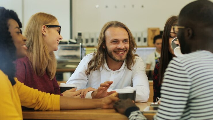 Camera focuses on a multiethnic group of friends through the window laughing and talking while drinking coffe sitting at a table in a cafe