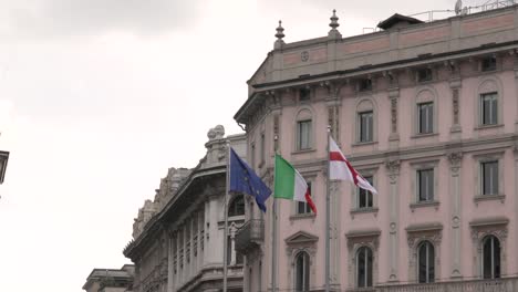 italian ,european and milan flags in the wind on the ancient palace in the center of milan