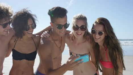 Mixed-race-group-of-friends-taking-selfies-on-the-beach-using-phone-camera