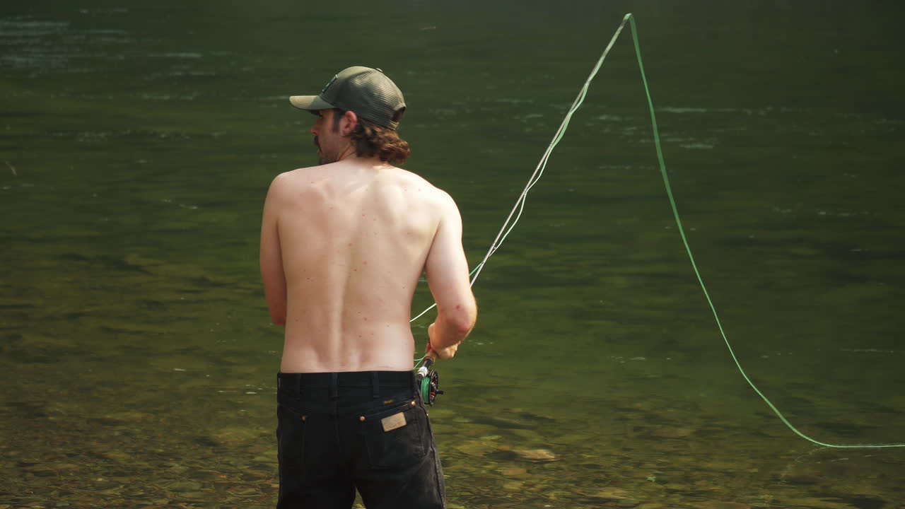 Pria Kaukasia memancing fly fishing di sungai yang mengalir di McDonald Creek, jarak menengah