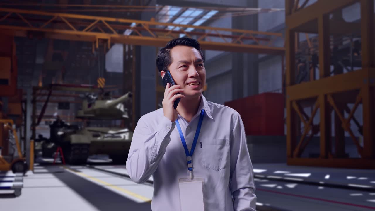 Pekerja Profesional Pria Asia Berdiri, Tank Militer Sedang Dibangun di Fasilitas Industri, Dia Mengangkat Telepon Dan Mulai Berbicara Dengannya
