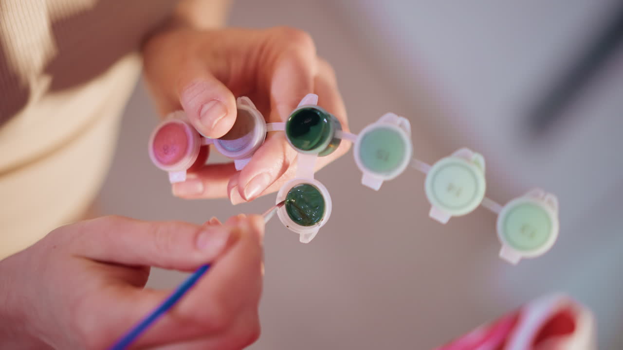 Close HandHeld Display Of Mini Paint Pots, Caucasian Creator Holds Assortment Of Pastel And Green Shades Toward Camera, Studio Background Blurred, Product And Craft Presentation Vibe
