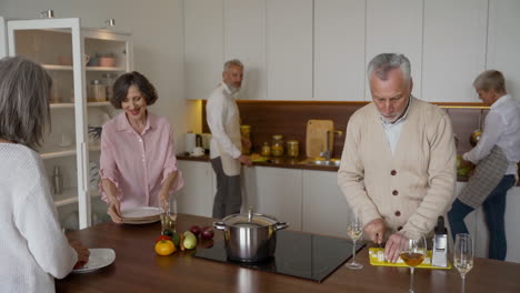 group of older friends cooking and talking in the kitchen while two men toasting with a glass of wine