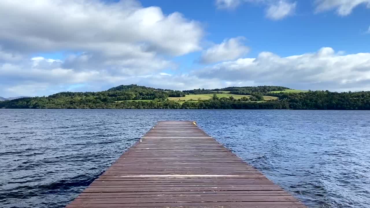 un muelle de madera en el lago ondulado frente a las colinas verdes con árboles, en escocia, reino unido