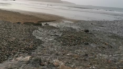 A-water-stream-and-tide-in-a-pebble-and-stone-beach-in-Broad-Haven,-West-Wales