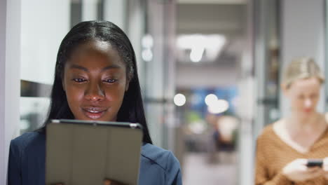 evening shot of young businesswoman standing in corridor of modern office using digital tablet