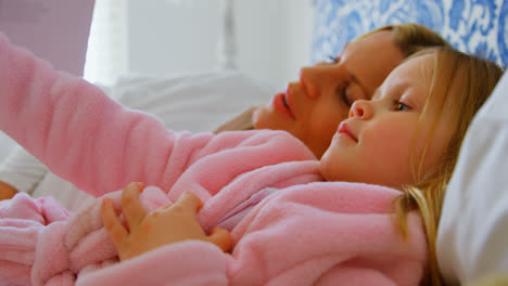 Vista-Lateral-De-Una-Joven-Madre-Caucásica-Y-Su-Hija-Leyendo-Un-Libro-De-Cuentos-En-La-Cama-En-Una-Cómoda-Casa-4k