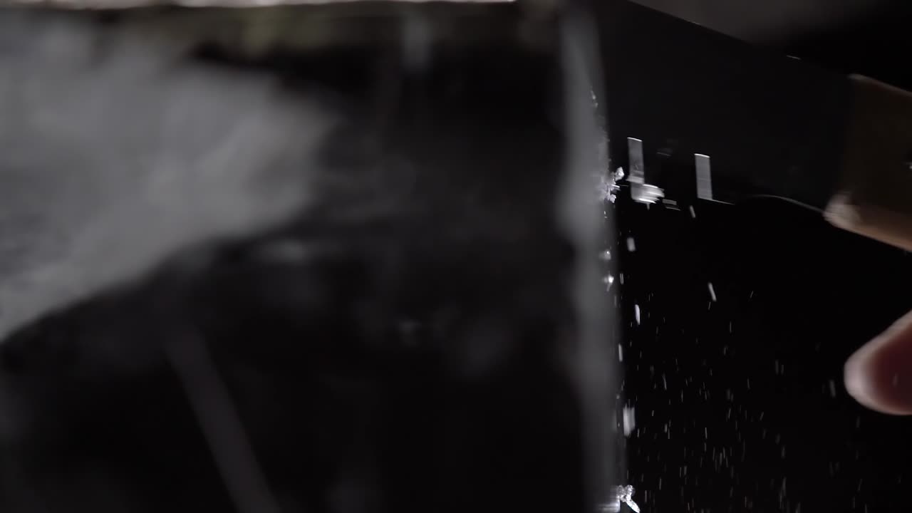 A bartender is cutting the ice block to smaller pieces for cocktail service by using a long toothed knife.