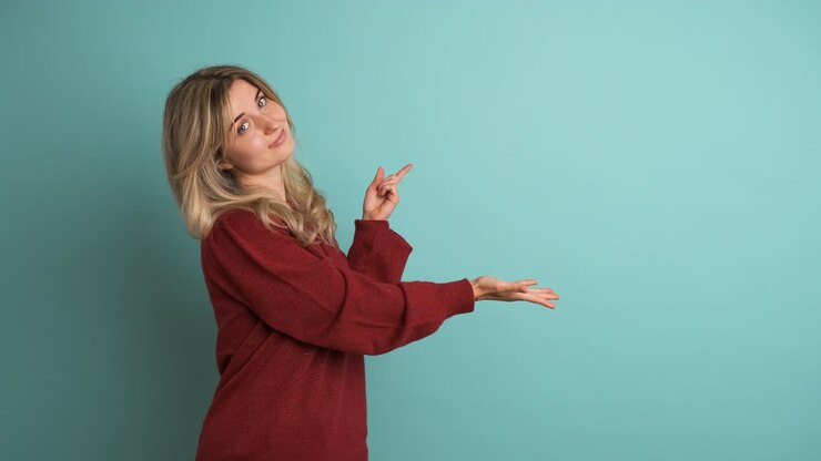 Happy young woman showing mockup space in blue studio