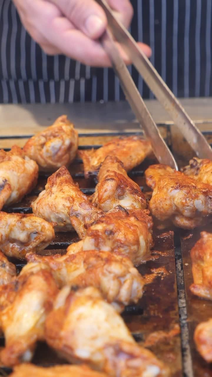 Chef che griglia deliziose alette di pollo su un barbecue caldo