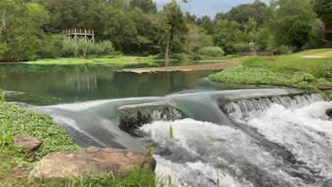 beautiful-park-in-background,-water-rushing-over-rocks-in-front-4k-30fps