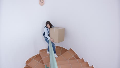 Happy-young-woman-carrying-a-box-upstairs