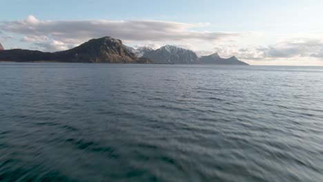 drone flies low over sea towards mountains at lofoten islan in northern norway