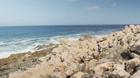 Hombre-Afroamericano-Con-Mochila-Caminando-Sobre-Las-Rocas-Mientras-Camina