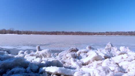 Vuelo-De-Drones-Sobre-Una-Gran-Pila-De-Fragmentos-De-Hielo-Y-Un-Río-Congelado-Hasta-Un-Bosque-Al-Otro-Lado