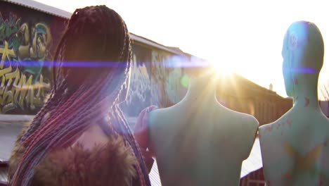 woman looking at mannequins in front of graffiti wall at sunset