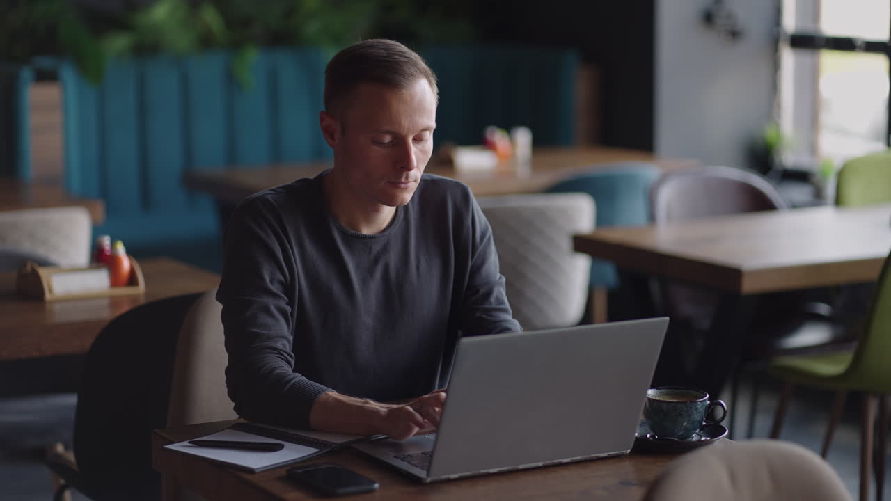apuesto empresario independiente con gafas trabajando diligentemente en una computadora portátil en una cafetería. hombre escribiendo en el teclado y buscando un nuevo trabajo en internet en una cafetería. concepto de negocio