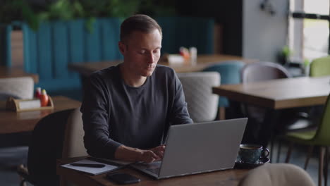 Hübscher-Freiberuflicher-Geschäftsmann-Mit-Brille,-Der-Fleißig-Am-Laptop-Im-Café-Arbeitet.-Mann-Tippt-Auf-Der-Tastatur-Und-Sucht-Im-Internet-Im-Café-Nach-Einem-Neuen-Job.-Geschäftskonzept