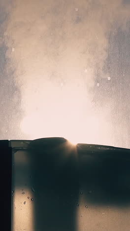 cu, slow motion, low angle shot: new air ionizer emits steam cloud to humidify and clean atmosphere near window closeup