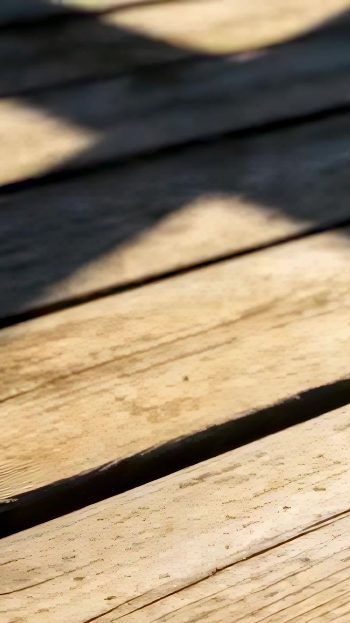 Vertical video: Shifting sunlight and camera wobble softening diagonal shadow across porch planks