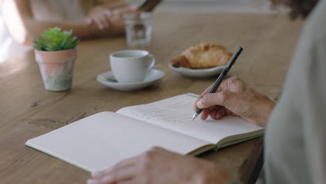 young woman hands writing to do list making notes in diary planning using journal reminder in coffee shop close up