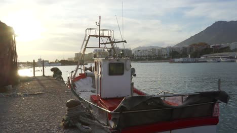 pequeño barco de pesca rojo y blanco amarrado en el puerto pesquero de marbella al atardecer, hermosa vista panorámica cinematográfica del barco de pesca español