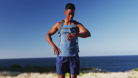 african american man cross country running using a smartwatch in countryside on a mountain