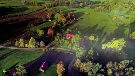 descending aerial shot of house in rural area with fields and colorful trees at sunset