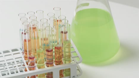 coloured liquid in flask with test tubes in stand on white background, slow motion